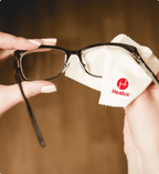 Person cleaning glasses with a cloth labeled 'Healux' on a blurred background