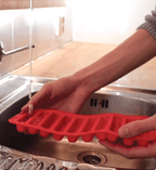 Red silicone ice cube tray being held over a sink