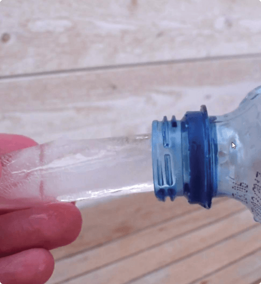 Clear plastic bottle with blue cap held by a hand on a wooden surface