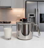 Stainless steel milk frothing pitcher on a kitchen counter with a glass of milk next to it.