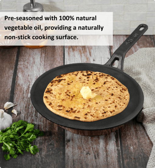 Black cast iron skillet with a cooked flatbread on a wooden surface, surrounded by fresh herbs and garlic.